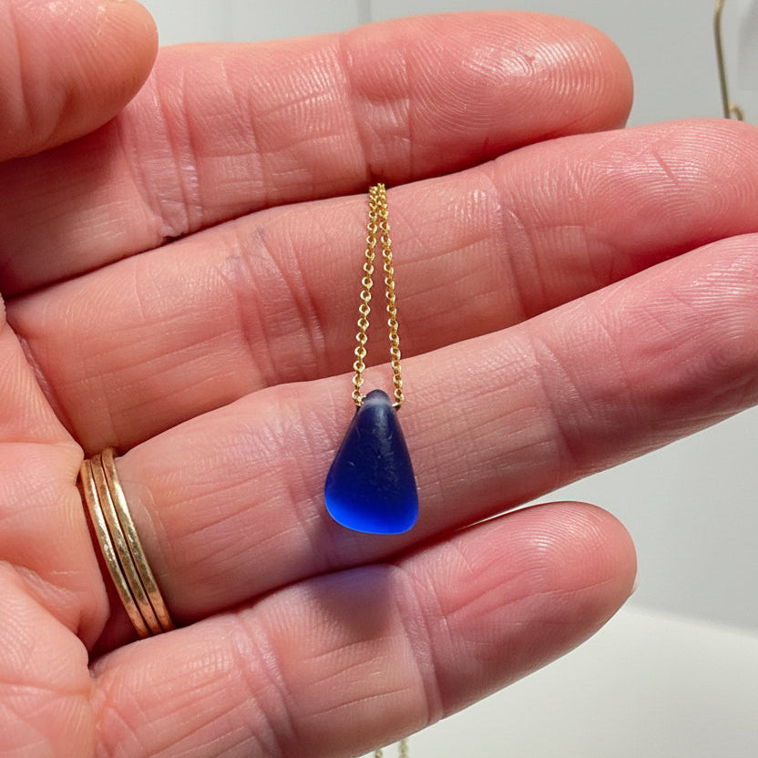 cobalt blue teardrop pendant on a gold chain against a white background